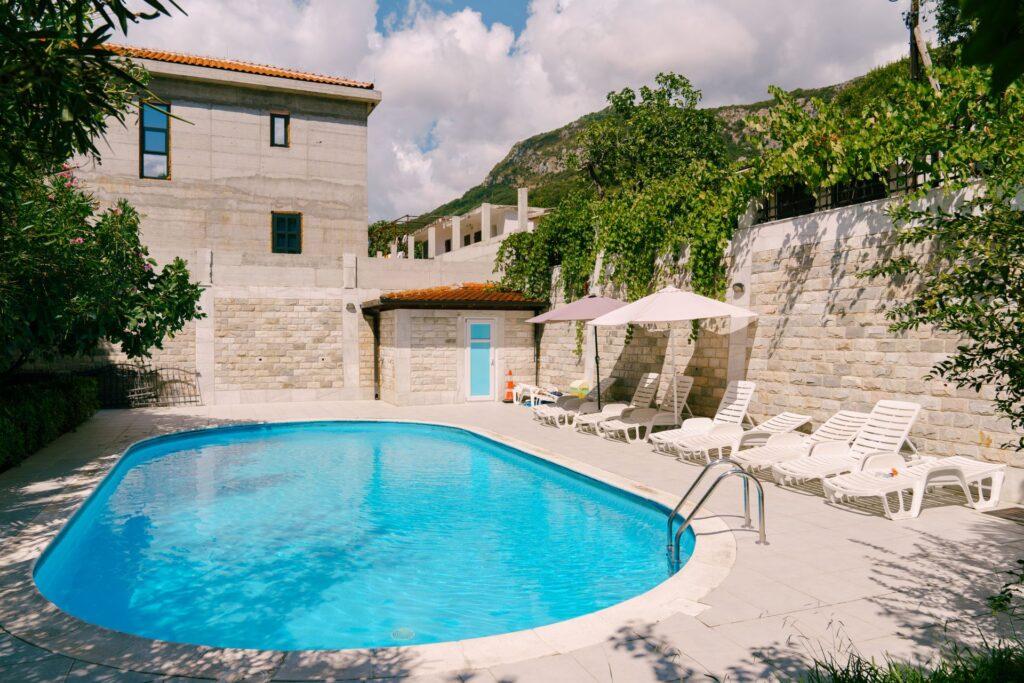 Stahlwandpool Oval eingebaut in mediterranem Garten mit Steinmauer und Sonnenliegen