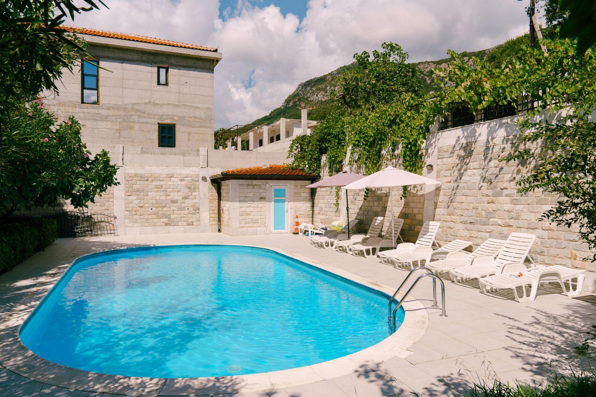Stahlwandpool Oval eingebaut in mediterranem Garten mit Steinmauer und Sonnenliegen